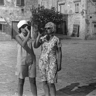 Two women looking through binoculars in a town square.