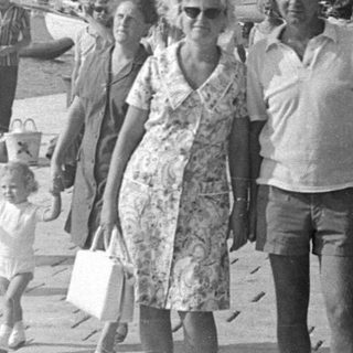 People walking along a harbor with a coastal town backdrop.