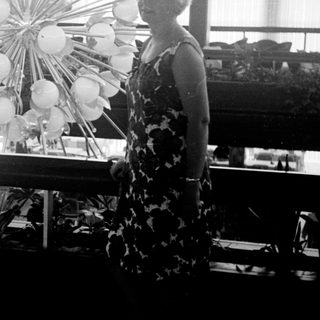 Woman stands near a floral display in a sunlit room.