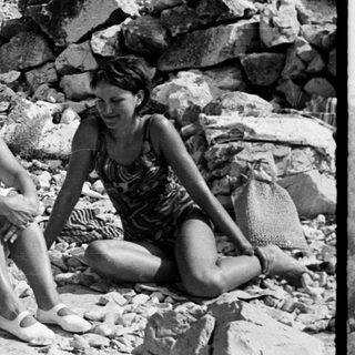 Three women sit on rocks in a rocky, natural landscape.