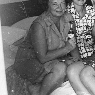 Three women with drinks sit on a bed.