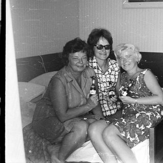 Three women with drinks sit on a bed.