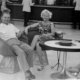 Couple relaxes in a lobby with a bar in the background.