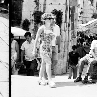 People walk past ancient ruins, a bustling street scene.