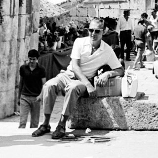 People walk past ancient ruins, a bustling street scene.