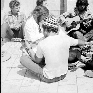 Group of men playing guitars outdoors, possibly performing.