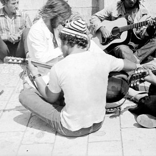 Group of men playing guitars outdoors, possibly performing.