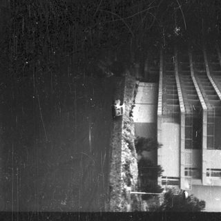 Black and white photo shows a building and a car.