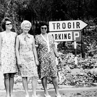 Three women pose near a "Trogir Parking" sign.