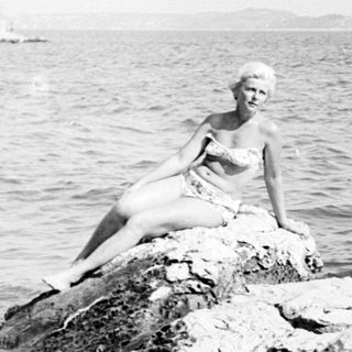 Woman sits on a rock in the water.