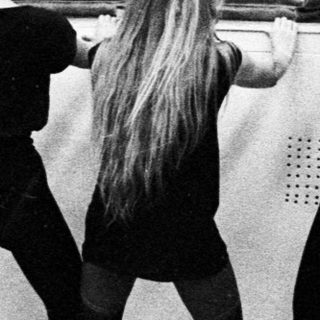 Ballet students stretching in a gymnasium, viewed from behind.