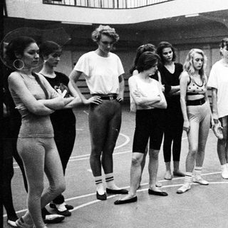 Ballet students observing a demonstration near a chair.