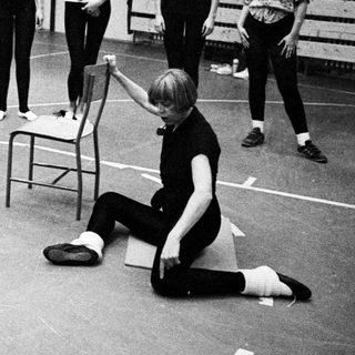 Ballet students observing a demonstration near a chair.