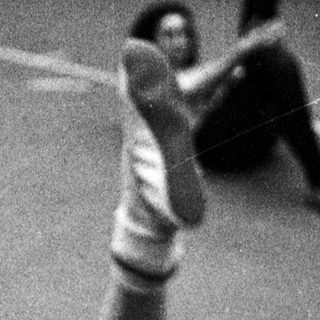 Here's a brief summary of the image: Gymnast practicing a floor exercise in a black and white photo.