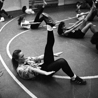 Here's a brief summary of the image: People exercising, performing leg raises in a circular room.