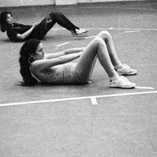 Here's a brief summary of the image: Two people are exercising on a dark, tiled floor.