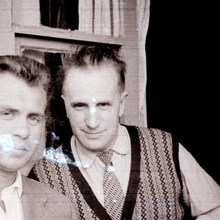 Two men standing outdoors, dressed in vintage clothing.