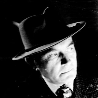 Man in a hat stands near a bookshelf.