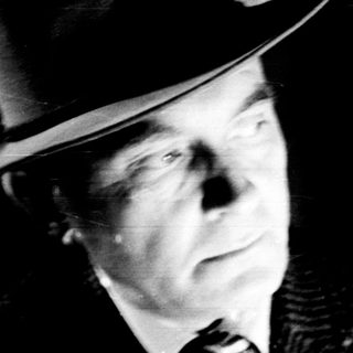 Man in a hat stands near a bookshelf.
