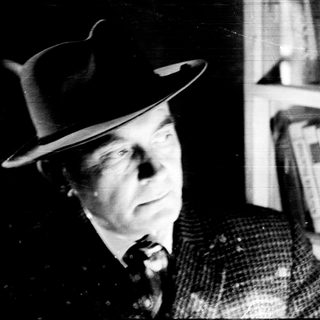 Man in a hat stands near a bookshelf.