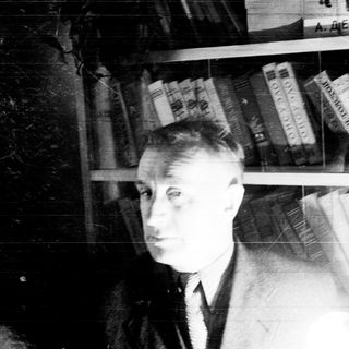 Man stands near a bookshelf in a black and white photo.