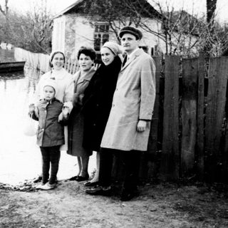 Family stands near floodwaters, appearing displaced or observing.