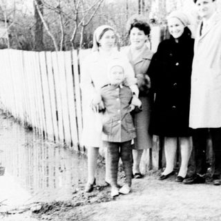 Family stands near floodwaters, appearing displaced or observing.