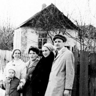Family stands near floodwaters, appearing displaced or observing.