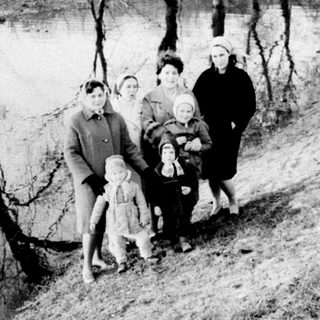 Group of people standing near a riverbank in winter.
