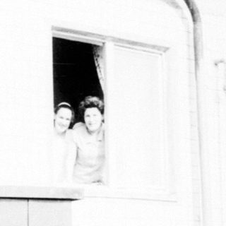 Here's a brief summary of what the image shows: People peering out of a window, attached to a building.