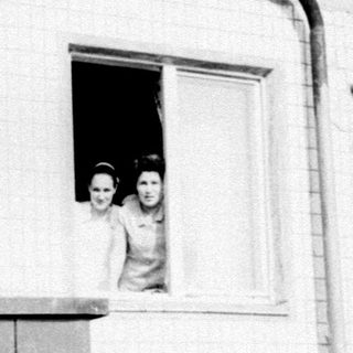 Two young girls peering out of a window.