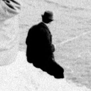 Child stands in snow; people in background.