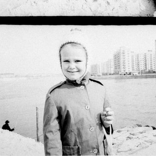 Child stands in snow; people in background.