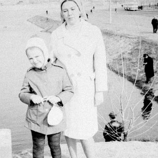 Woman stands with child, bag nearby on snowy ground.