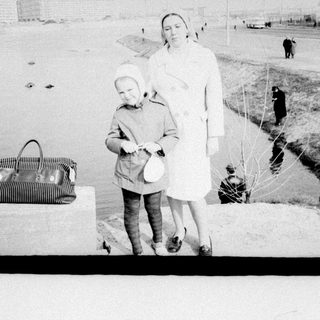 Woman stands with child, bag nearby on snowy ground.