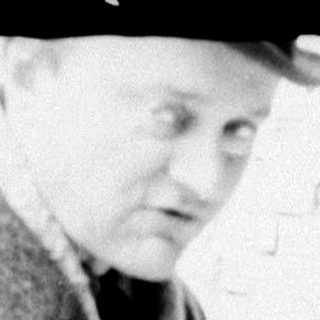 Man in coat examining something near brick wall.