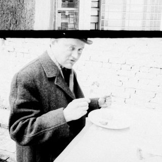 Man in coat examining something near brick wall.