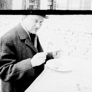 Man in coat examining something near brick wall.