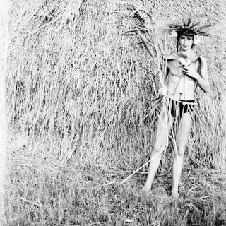 Man in ceremonial attire stands before a large haystack.