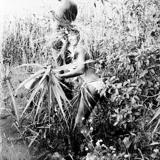 Man stands in tall vegetation near a body of water.