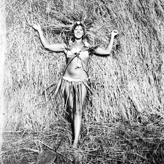 Woman in traditional dress stands amidst tall grass.