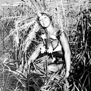 Woman sits amidst tall reeds near a lake.