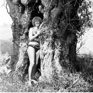Woman posing playfully next to a large tree.