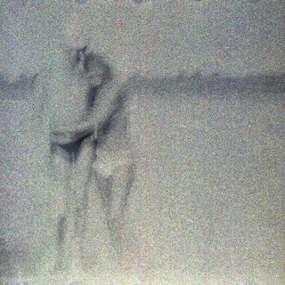 Person standing near a body of water, grainy image.