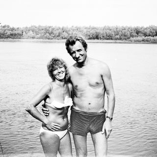 Couple in swimwear stands near a body of water.