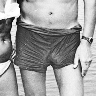 Couple in swimwear stands near a body of water.