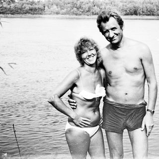 Couple in swimwear stands near a body of water.