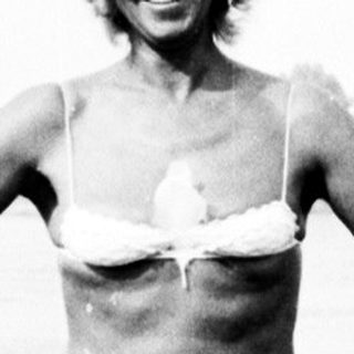 Woman in bikini stands on shore near water.