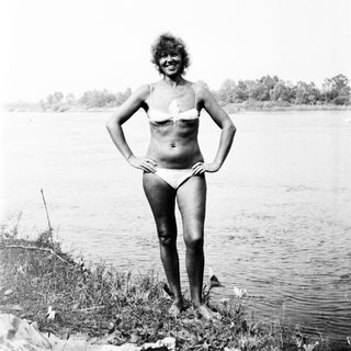 Woman in bikini stands on shore near water.