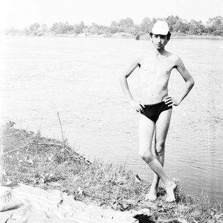 Boy stands near a body of water, wearing swimwear.